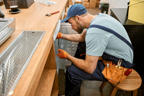Bearded young man repairing fridge in cafe