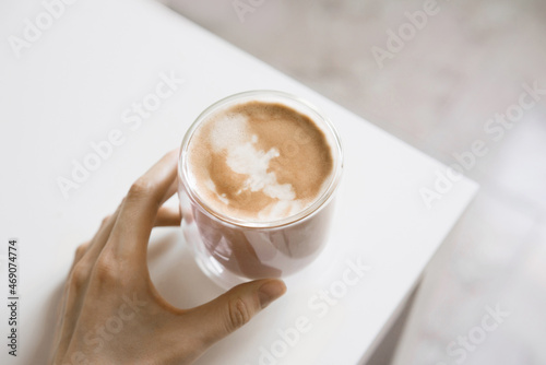 Female hand holding cup of home made coffee. Cappuccino with milk