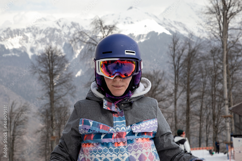 Portrait of a girl in snowboard clothes against a background of mountains
