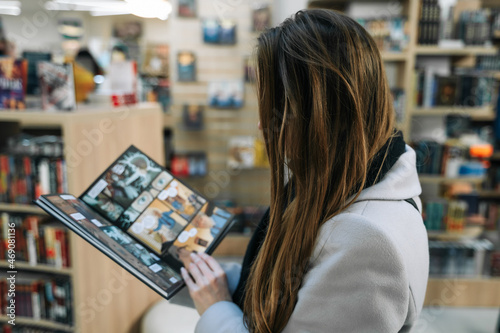A beautiful young woman chooses a comic book for a gift in a bookstore to buy it. Woman stands with her back, comic book is open, blured.