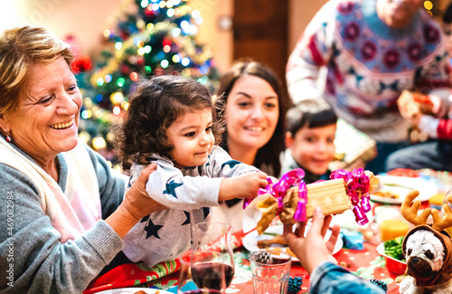 Large multi generation family having fun at christmas home supper - Winter holiday x mas concept with parents and children opening gifts together at dinner - Focus on little daugther - Warm filter