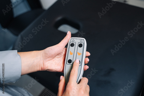 Beautiful female hands with manicure hold a remote control for adjusting the position from the massage table (bed) located in the SPA room. Presses the buttons.
