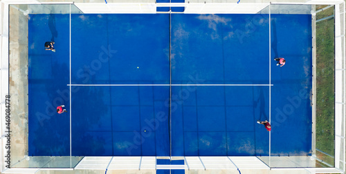View from above, stunning aerial view of some people playing on a blue padel court. Padel is a mix between Tennis and Squash. It's usually played in doubles on an enclosed court.