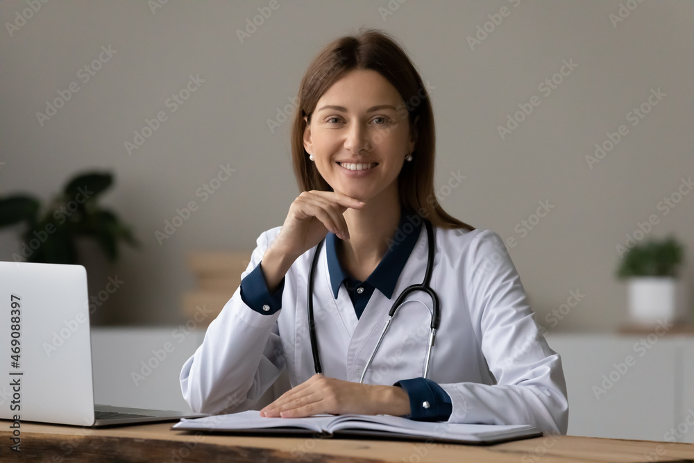 Head shot portrait smiling young female therapist doctor in white uniform with stethoscope sitting at work desk in hospital office, confident happy woman professional gp looking at camera, healthcare Head shot portrait smiling young female therapist doctor in white uniform with stethoscope sitting at work desk in hospital office, confident happy woman professional gp looking at camera, healthcare