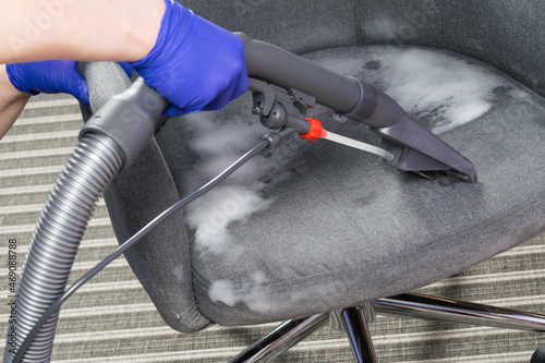 wet cleaning of the chair with a cleaning vacuum cleaner and thick foam, hands in protective gloves photo