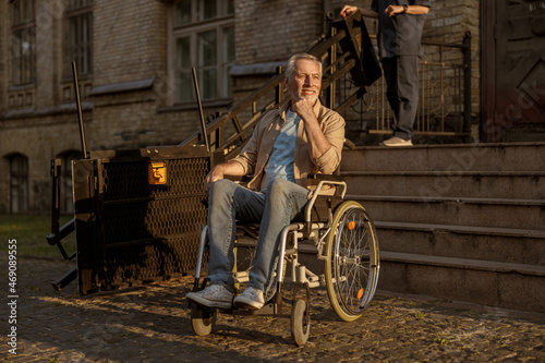 Full length shot of cheerful mature disabled man in wheelchair smiling away while spending time alone outdoors at sunset
