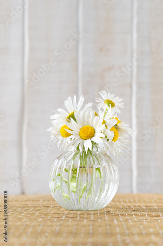Camomile in glass vase on a wicker mat against white wooden wall