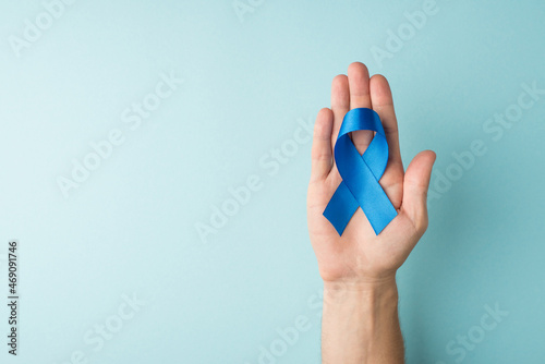 First person top view photo of male hand holding blue silk ribbon in palm symbol of prostate cancer awareness on isolated pastel blue background with blank space photo