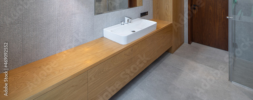 Interior of bathroom in luxury flat. Grey and wooden design. White sink.