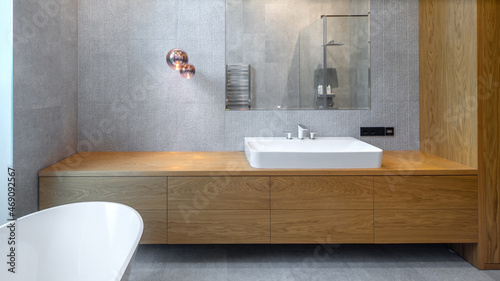 Interior of bathroom in luxury flat. Grey and wooden design. White sink.
