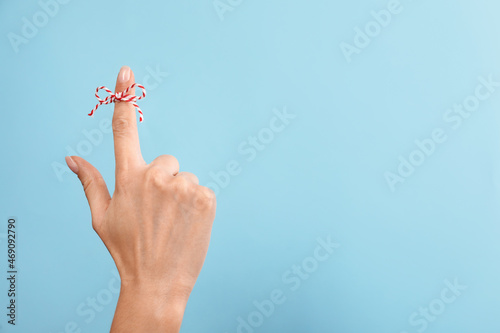 Woman showing index finger with tied bow as reminder on light blue background  closeup. Space for text