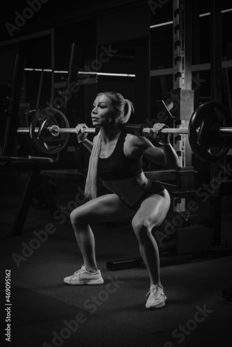 A fit woman is squatting with a barbell near the squat rack in a gym.