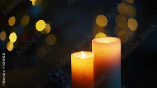 Close up of two burning candles over blur christmas lights. Garland lighting and christmas decoration at home. Cozy festive atmosphere.