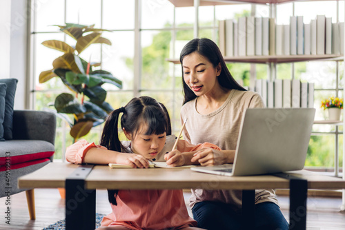 Portrait happy love asian family mother teach little daughter asian girl learning and study on laptop.Mom and asian girl writing with book and pencil making homework in homeschool at home.Education