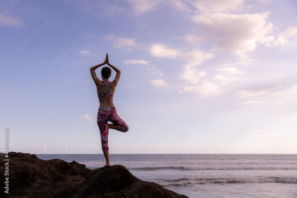 Outdoor yoga. Vrikshasana asana. Woman practicing tree pose on the rock ...