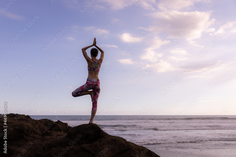 Outdoor yoga. Vrikshasana asana. Woman practicing tree pose on the rock ...