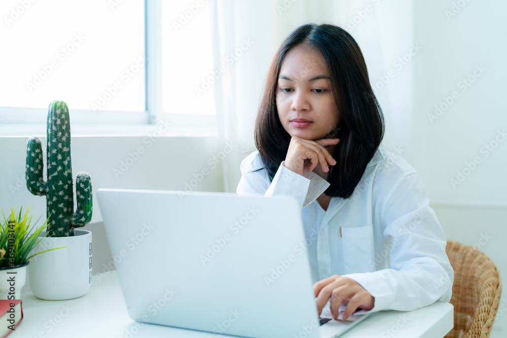 Portrait Cute Asian teen with long hair Wearing a white shirt, sitting online studying with a laptop on the bedroom table with a thoughtful face. Portrait Cute Asian teen with long hair Wearing a white shirt, sitting online studying with a laptop on the bedroom table with a thoughtful face.