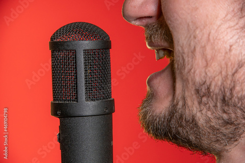 Singing Male Mouth In Front Of A Microphone On A Red Background. Broadcast, Radio and Podcasts. Singing Songs and Recording into the Microphone.