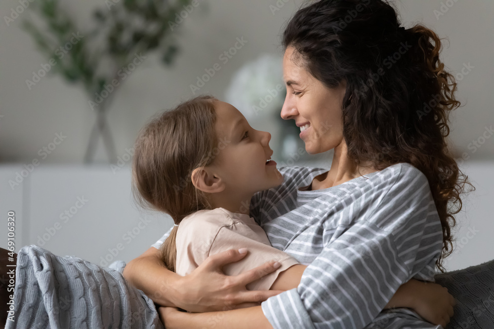 Close up profile of happy caring mother and little daughter hugging cuddling enjoying tender moment, looking in eyes and talking, smiling mom with kid spending leisure time at home together Close up profile of happy caring mother and little daughter hugging cuddling enjoying tender moment, looking in eyes and talking, smiling mom with kid spending leisure time at home together