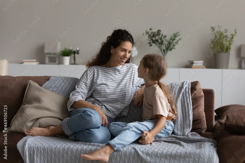 Smiling mother with little daughter talking, sitting on comfortable couch, happy caring mom and adorable girl child sharing news, spending leisure time at home together, good trusted relationship