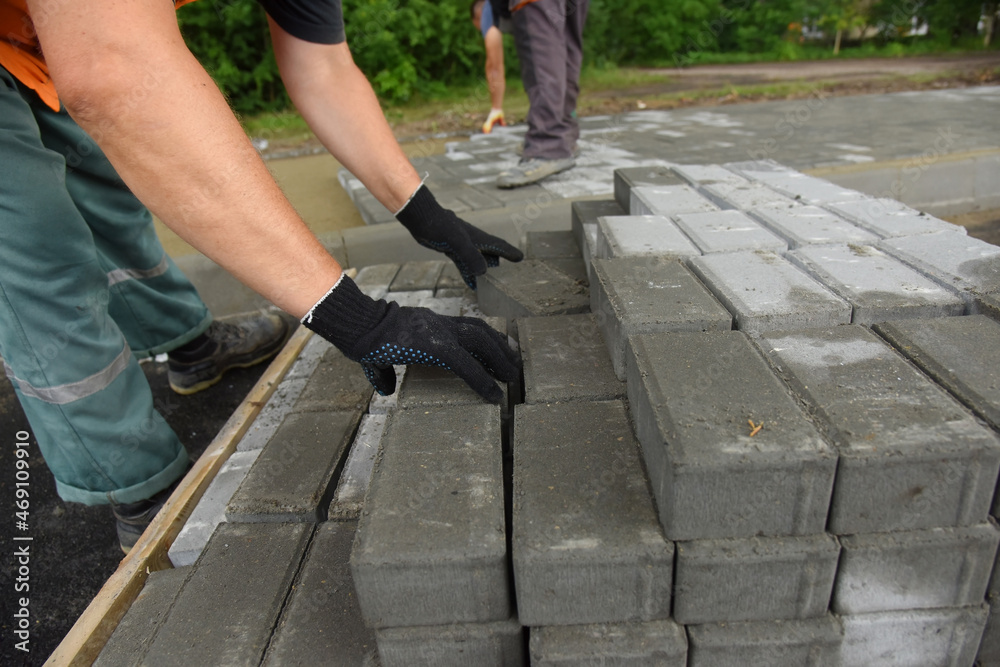 A worker removes concrete tiles from a pallet, builds a parking lot for cars. A worker removes concrete tiles from a pallet, builds a parking lot for cars.