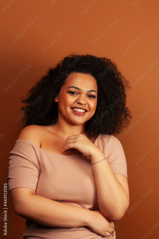 pretty young african american woman with curly hair posing cheerful gesturing on brown background, lifestyle people concept pretty young african american woman with curly hair posing cheerful gesturing on brown background, lifestyle people concept