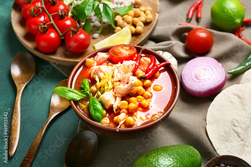 Bowl with tasty pozole soup and ingredients on green background