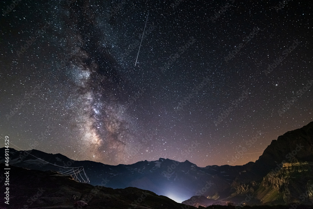 the Milky way galaxy and stars over the Italian French Alps. Night sky on majestic snowcapped mountains and glaciers. Meteor shower on the right