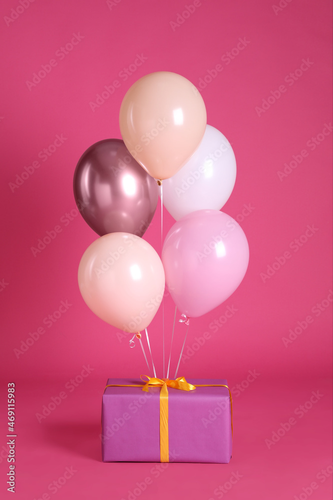 One gift box and balloons near bright pink background