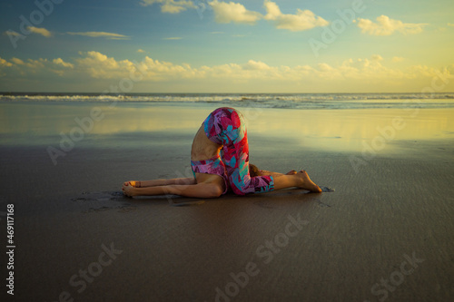 Beach yoga. Caucasian woman practicing Karnapidasana. Ear pressure pose.  Knee to ear pose. Inverted asana. Yoga retreat. Flexible spine. Healthy lifestyle. Slim fit body. Copy space. Bali photo