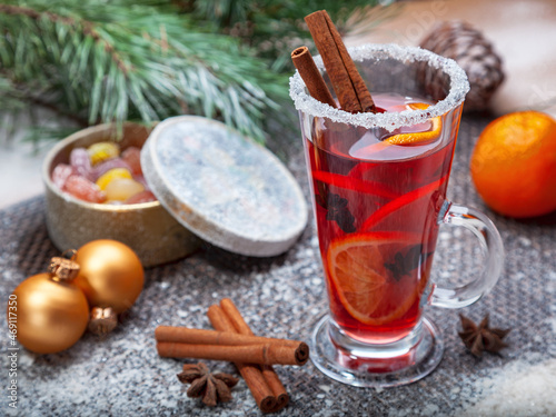 Christmas hot mulled wine with a slice of orange and spices. A glass cup with a hot traditional drink on a snowy background in festive decorations. Evening mood and decoration 