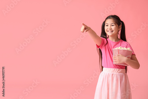 Cute girl with bucket of popcorn pointing at something on pink background