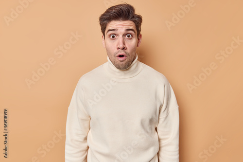 Wallpaper Mural Horizontal shot of impressed young brunet man gasps from wonder looks with eyes full of disbelief hears stunning shocking rumor wears casual turtleneck isolated over beige background. Omg concept Torontodigital.ca