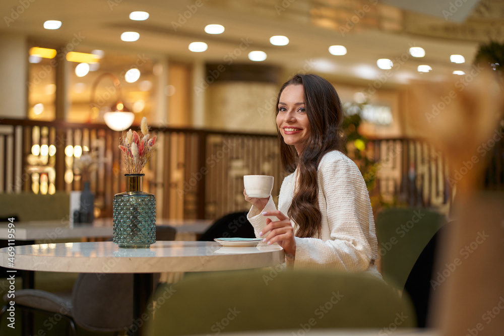 Young beautiful stylish woman in white blazer with cup od coffee sitting in restaurant Young beautiful stylish woman in white blazer with cup od coffee sitting in restaurant