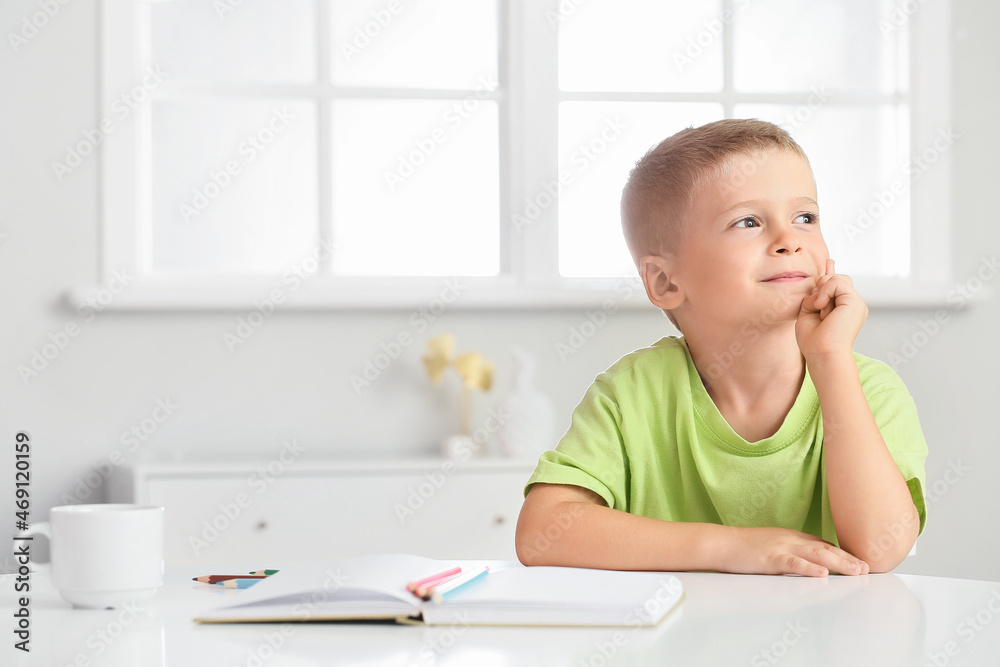 Thoughtful little boy sitting at table in room Thoughtful little boy sitting at table in room
