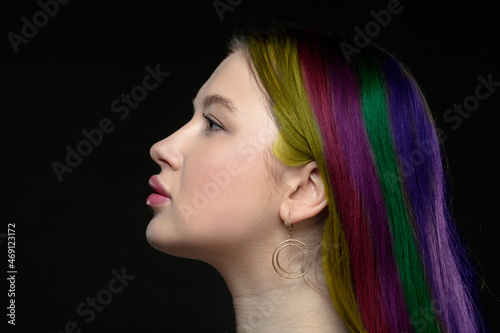 Profile of a young female model with perfect sensual lips and multi-colored strands of hair on a black background. Beautiful facial skin, augmentation of female lips, glamorous elegance.