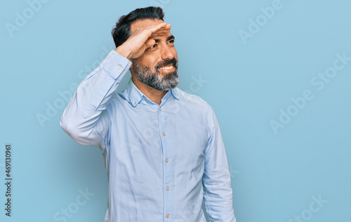 Middle aged man with beard wearing business shirt very happy and smiling looking far away with hand over head. searching concept. © Krakenimages.com