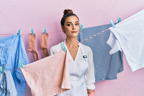 Beautiful brunette young woman washing clothes at clothesline relaxed with serious expression on face. simple and natural looking at the camera.