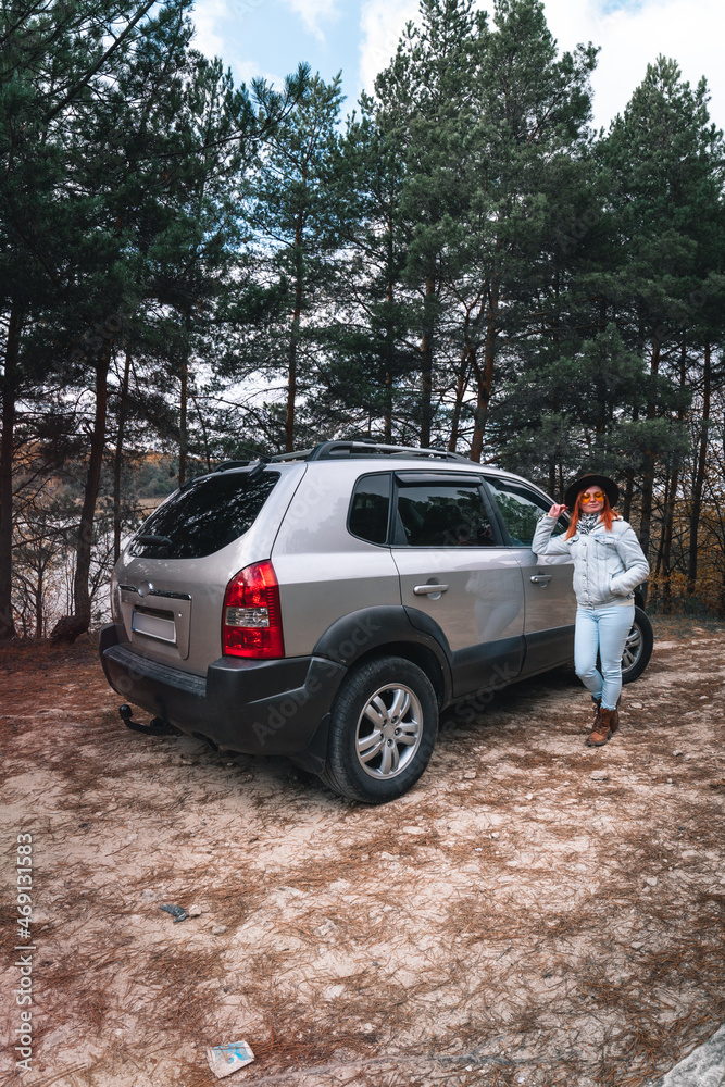 Woman tourist travel by SUV car for road trip in autumn. The traveler parking the car and enjoy beautiful scenery of forest in the background. Discovery and exploration. Vertical photo Woman tourist travel by SUV car for road trip in autumn. The traveler parking the car and enjoy beautiful scenery of forest in the background. Discovery and exploration. Vertical photo