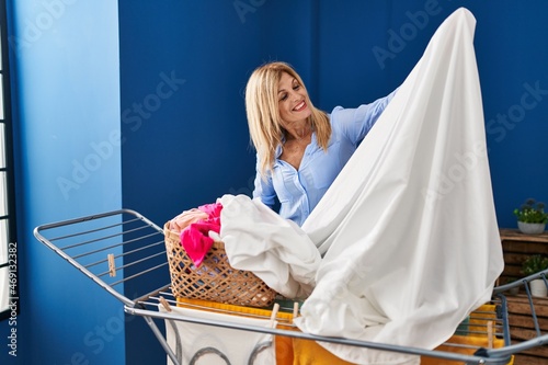 Middle age blonde woman smiling confident hanging clothes on clothesline at laundry room photo