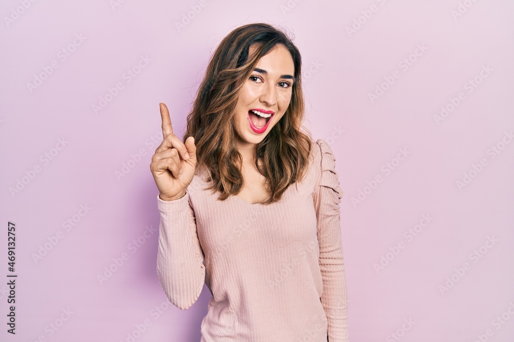 Young hispanic girl wearing casual clothes smiling with an idea or question pointing finger up with happy face, number one