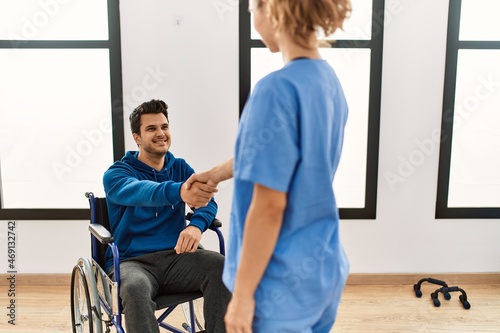 Young disabled man and physiotherapist smiling happy shaking hands at the clinic.
