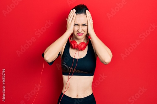 Obraz na plátně Young hispanic girl wearing gym clothes and using headphones suffering from headache desperate and stressed because pain and migraine