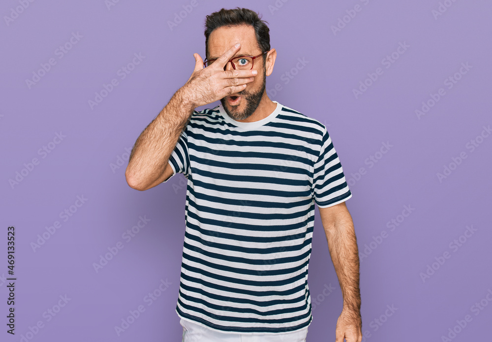 Middle age man wearing casual clothes and glasses peeking in shock covering face and eyes with hand, looking through fingers with embarrassed expression. Middle age man wearing casual clothes and glasses peeking in shock covering face and eyes with hand, looking through fingers with embarrassed expression.