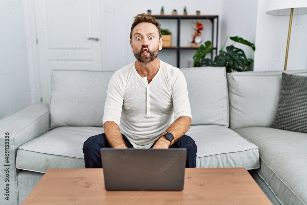 Middle age man using laptop at home making fish face with lips, crazy and comical gesture. funny expression. Middle age man using laptop at home making fish face with lips, crazy and comical gesture. funny expression.