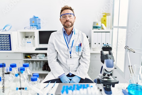 Middle age man working at scientist laboratory with serious expression on face. simple and natural looking at the camera.