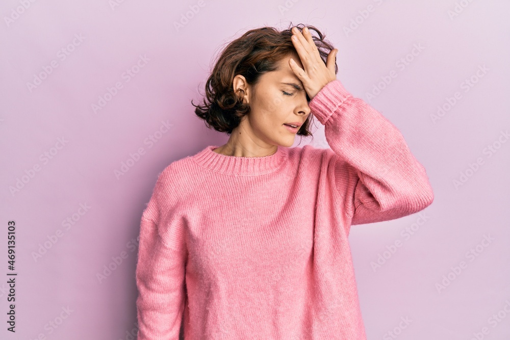 Young brunette woman wearing casual winter sweater surprised with hand on head for mistake, remember error. forgot, bad memory concept.