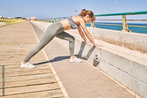 Young caucasian woman wearing sportswear stretching at seaside