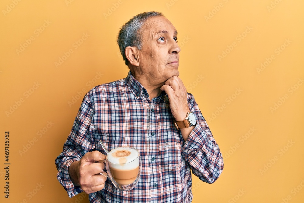 Handsome senior man with grey hair drinking a cup coffee with hand on chin thinking about question, pensive expression. smiling with thoughtful face. doubt concept. Handsome senior man with grey hair drinking a cup coffee with hand on chin thinking about question, pensive expression. smiling with thoughtful face. doubt concept.