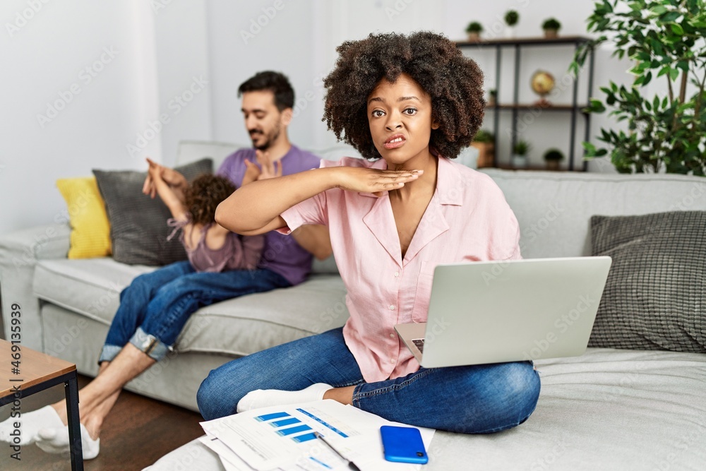 Mother of interracial family working using computer laptop at home cutting throat with hand as knife, threaten aggression with furious violence Mother of interracial family working using computer laptop at home cutting throat with hand as knife, threaten aggression with furious violence